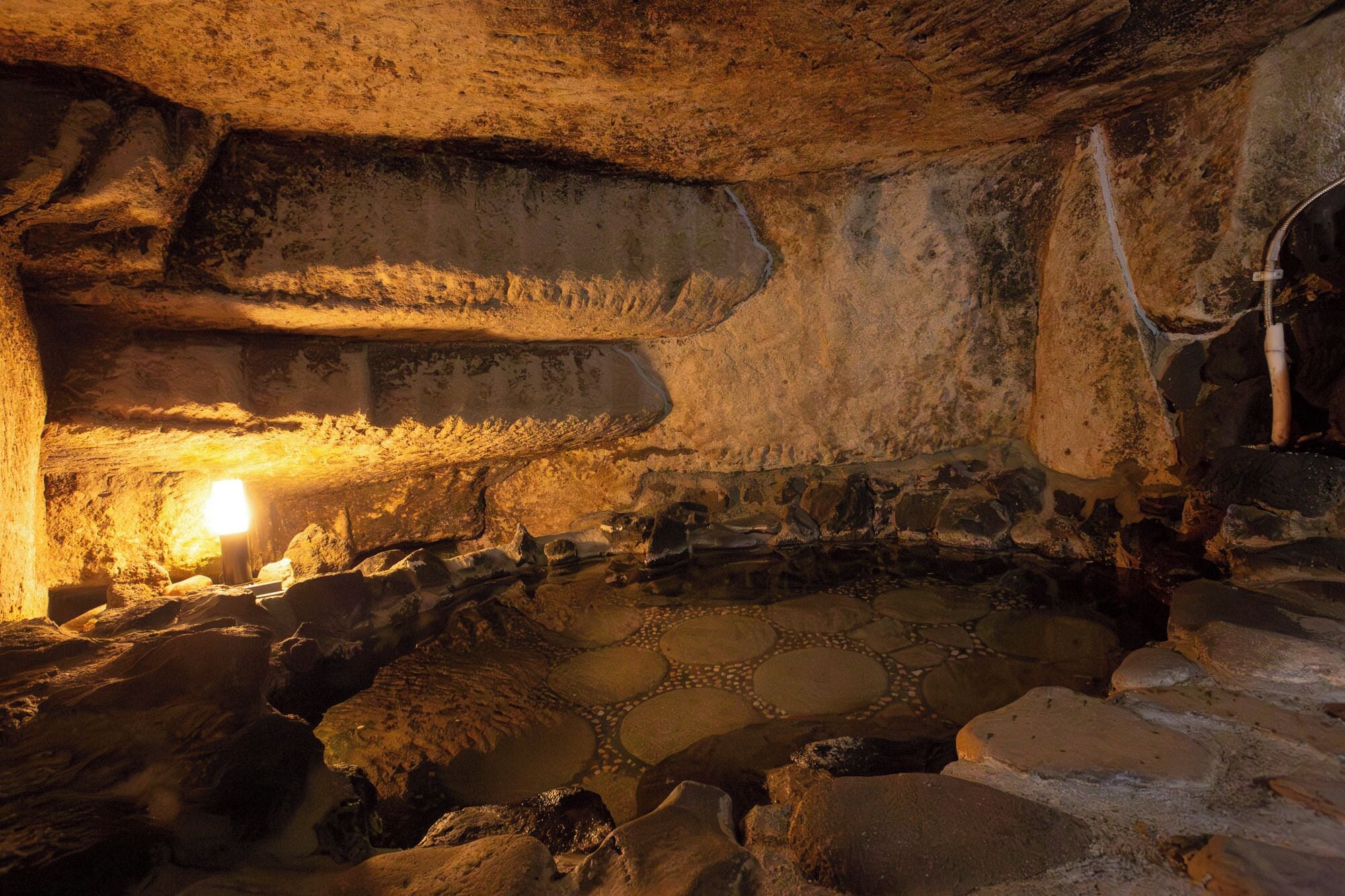 A cave interior with a central water feature, stone walls, and a light source.