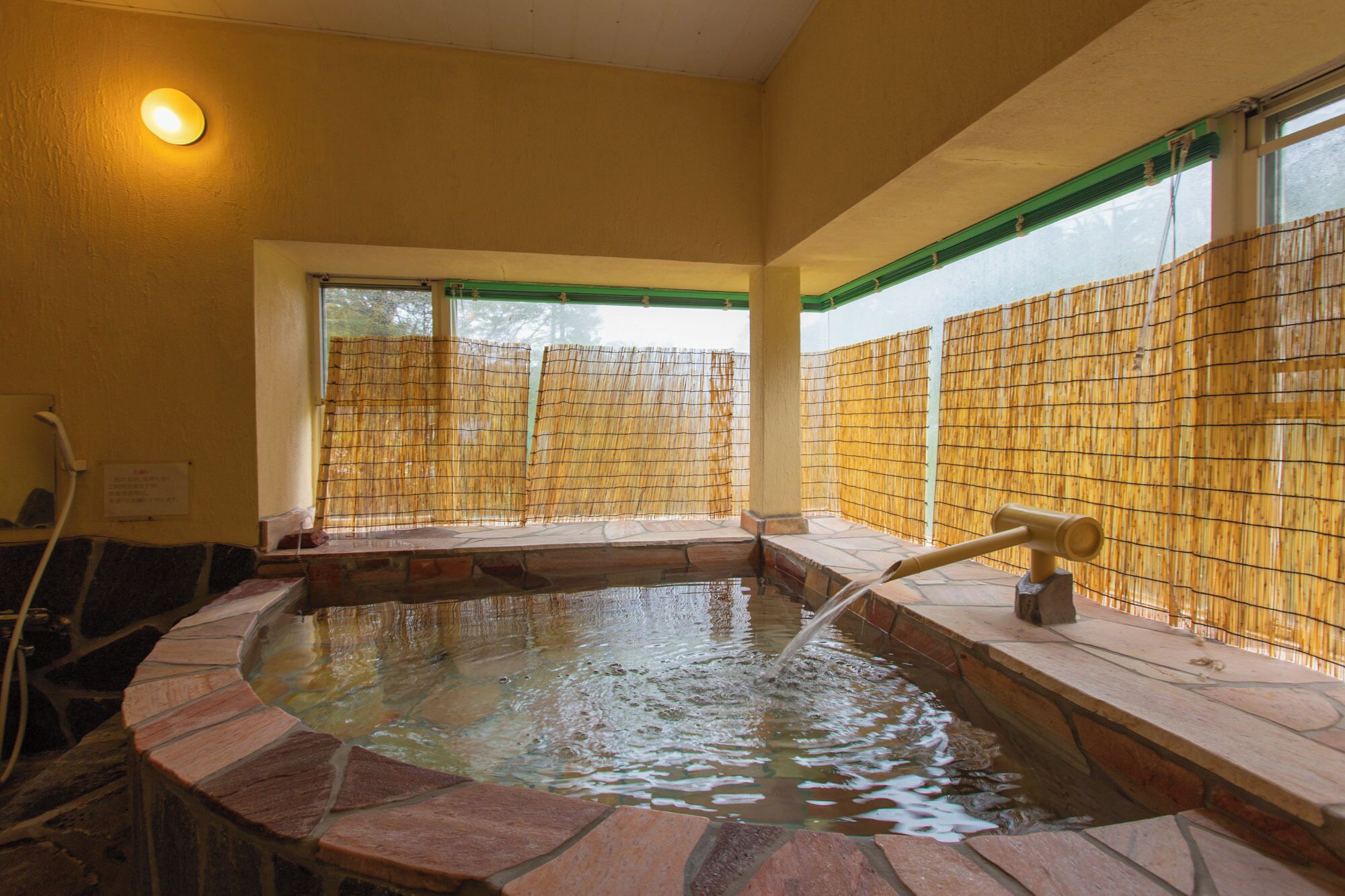A hot tub with a stone surround, a bamboo fence, and a window with a view.