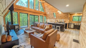 Un interior de cabaña espacioso con una amplia sala de estar, una cocina y una chimenea.