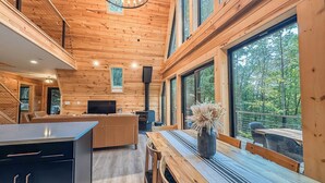 Interior moderno de una cabaña de troncos con comedor, cocina y grandes ventanales que dan a una vista del bosque.