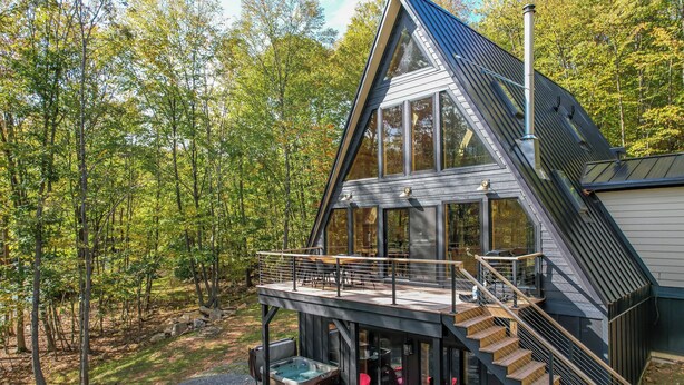 Una cabaña moderna con una terraza acristalada, un jacuzzi y una escalera que lleva a un segundo nivel.