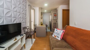 Een moderne woonkamer met een flatscreen televisie, een bank en een eethoek met stoelen.