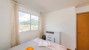 Une chambre à coucher avec un lit, une fenêtre avec des rideaux, une porte en bois et une commode blanche.
