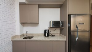 Une cuisine compacte équipée d’un réfrigérateur en acier inoxydable, d’un four à micro-ondes et d’une machine à café posés sur le plan de travail.