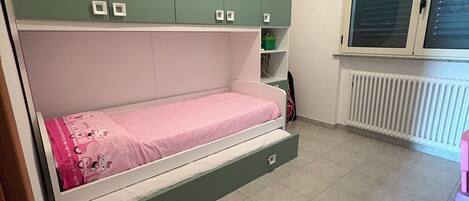 Un dormitorio con cama, armarios verdes, una ventana y un radiador.