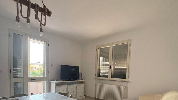 A compact living space with a dining table, a sofa, a television, and a radiator. - Sofia House, close to the center and the sea (Torre San Giovanni)