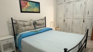 A bedroom with a bed, a nightstand, a chair, a wardrobe, and a painting on the wall. - Sofia House, close to the center and the sea (Torre San Giovanni)