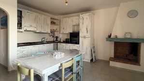 A kitchen with white cabinets, a marble countertop, a hanging rope chandelier, and a brick fireplace. - Sofia House, close to the center and the sea (Torre San Giovanni)
