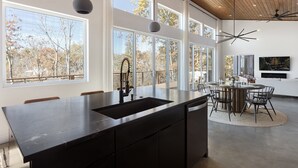 Una cocina moderna con una isla grande, un comedor con una mesa redonda y amplias ventanas que dan a un paisaje de árboles.