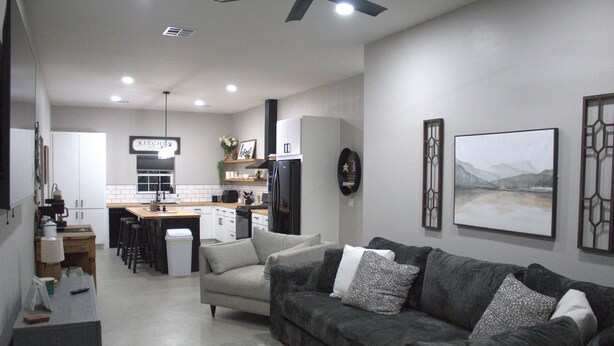 Un salon moderne avec un canapé gris, une table basse et un coin cuisine à l’arrière-plan.