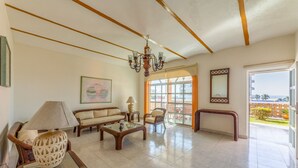 A spacious living room with a sofa, armchair, and coffee table, a chandelier, and a large window offering a view of the outdoors. - Quinta Nayarit (Bucerías)