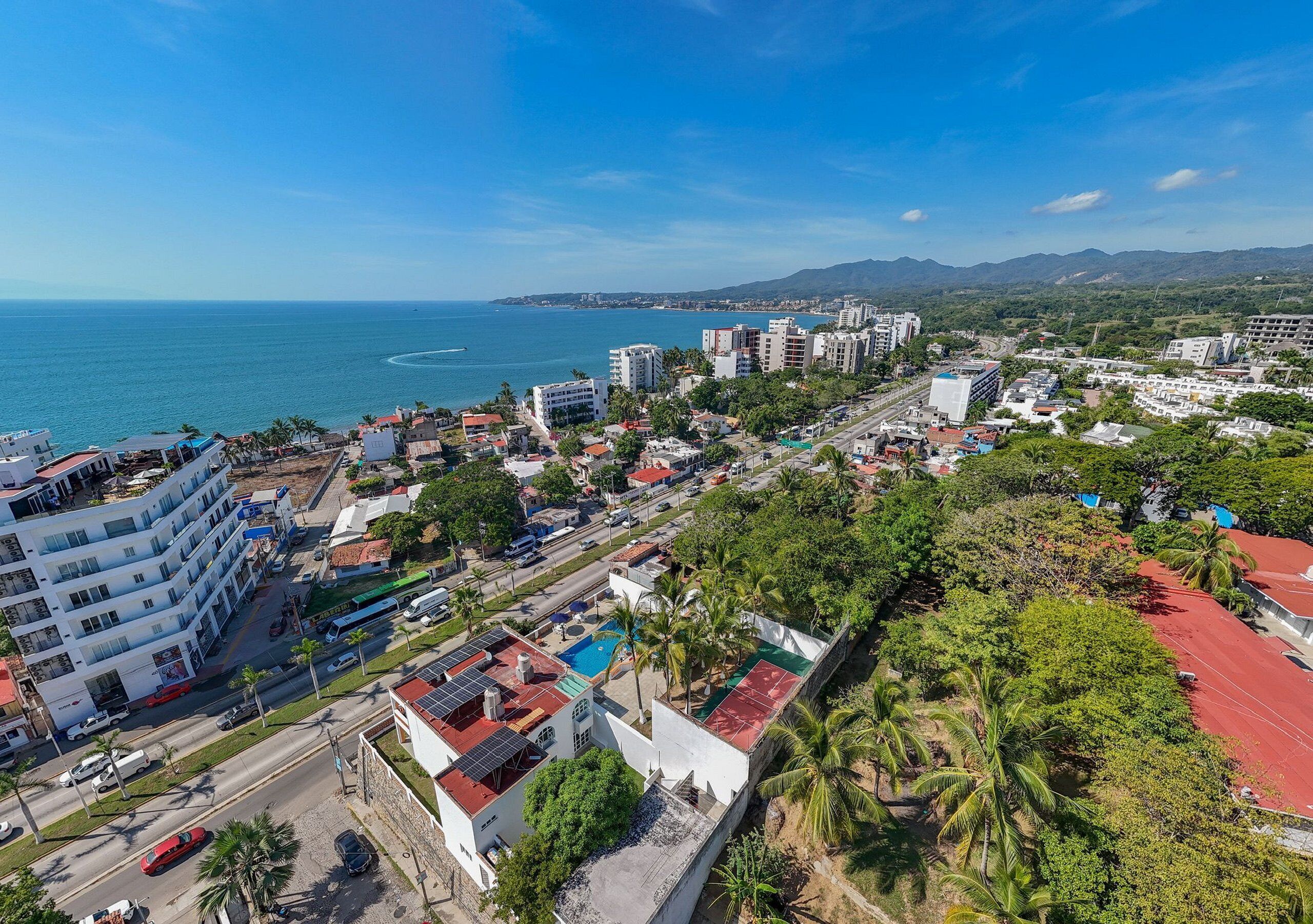 Un paisaje urbano costero con edificios modernos, un cielo azul despejado y vista al mar.