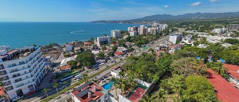 Un paisaje urbano costero con edificios modernos, un cielo azul despejado y vista al mar.