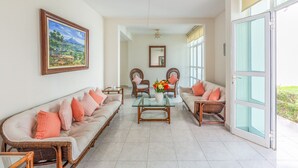 A spacious living room with a glass coffee table, two sofas, wicker chairs, and a large window offering a view of greenery. - Quinta Nayarit (Bucerías)