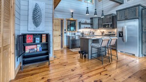 A spacious kitchen with wooden floors, a central island with bar stools, stainless steel appliances, and a large window above the island. - Wellness Retreat! Peloton, Hot Tub, Sauna, Outdoor Gym, Views, and 2 King Suites (Cherry Log)