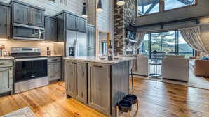 A modern kitchen with built-in appliances, a large island, and a stone fireplace. - Wellness Retreat! Peloton, Hot Tub, Sauna, Outdoor Gym, Views, and 2 King Suites (Cherry Log)