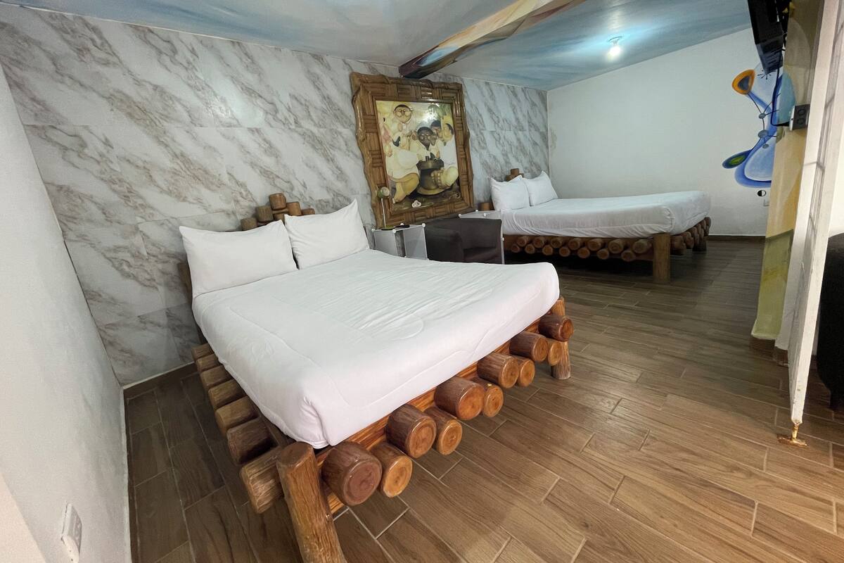 Une chambre à coucher avec un lit reposant sur des troncs d’arbres, une tête de lit en bois, un mur en marbre et un tableau.