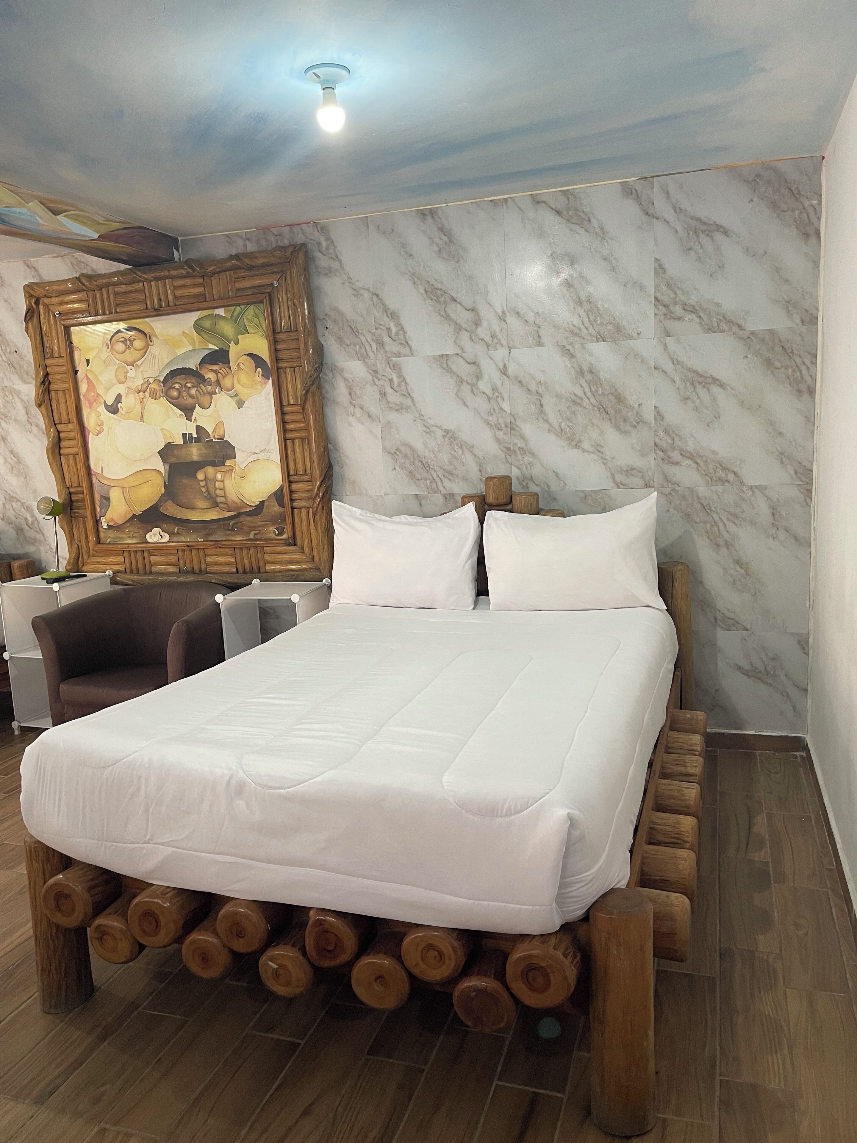 Habitación de hotel con cama, cabecera de madera, paredes de mármol y un cuadro en la pared.