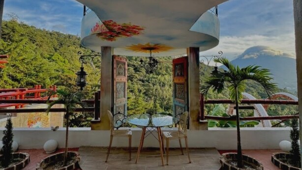 Un espace extérieur aménagé avec une zone de repos couverte, comprenant une table et des chaises, entouré de plantes en pot et offrant une vue sur un paysage montagneux.