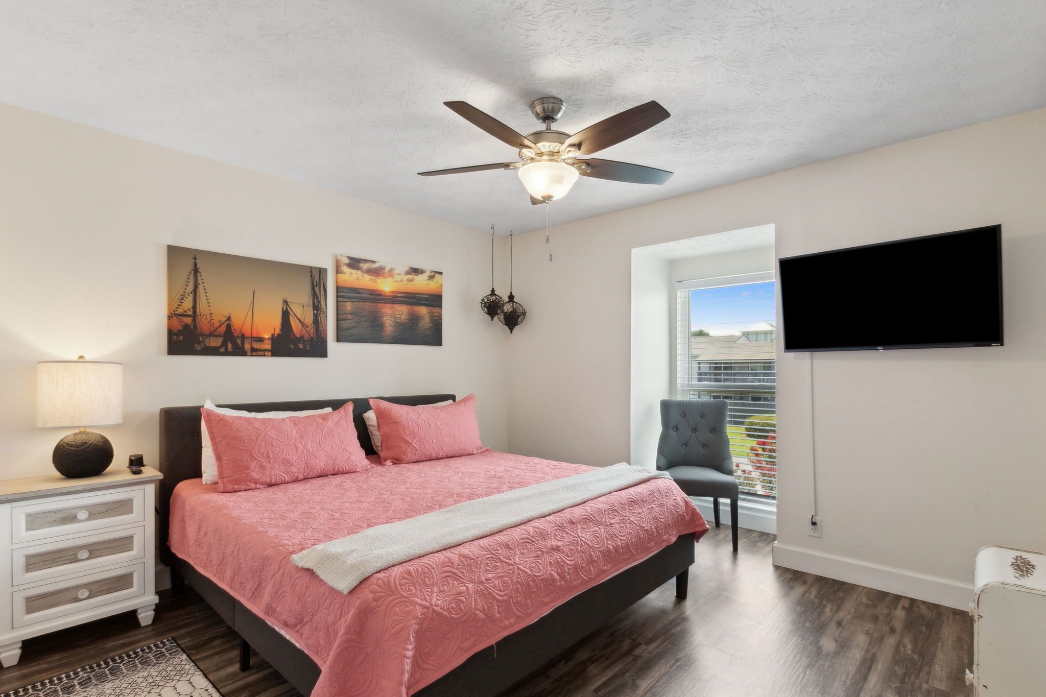 A bedroom with a bed, a ceiling fan, a TV, and artwork on the walls.