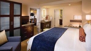 A hotel room with a large bed, a desk, a chair, a wardrobe, a bathroom, and a kitchenette.
