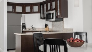 A modern kitchen with dark wooden cabinets, a stainless steel refrigerator, a microwave, and a coffee maker. There is a wooden bowl with apples on the counter.