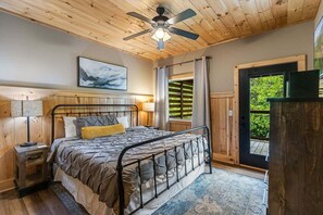 A bedroom with a bed, a ceiling fan, a window with curtains, a nightstand, and a painting on the wall. - The Sundrop - Relaxing Soaks, Fireside Drinks & Game Nights Near Ober Mountain (Gatlinburg)