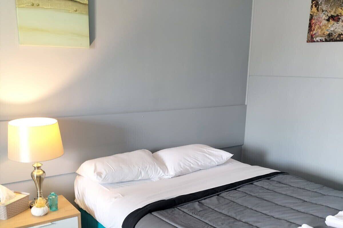 A neatly made bed with white and grey bedding, a bedside table with a lamp, and a small decorative item.