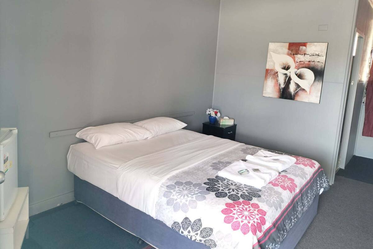 A bedroom with a bed, a nightstand, a wall-mounted artwork, and a door.