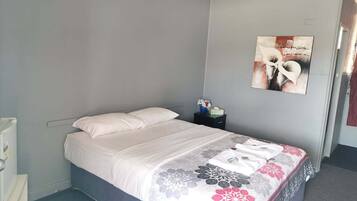 Un dormitorio con una cama, una mesita de noche, una obra de arte en la pared y una puerta.