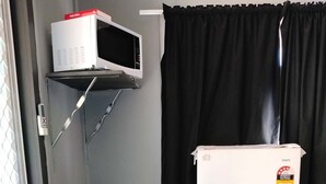 A compact kitchenette with a white refrigerator, a microwave, a kettle, and a small window with a curtain. - Maryborough Motel and Conference Center (Maryborough)