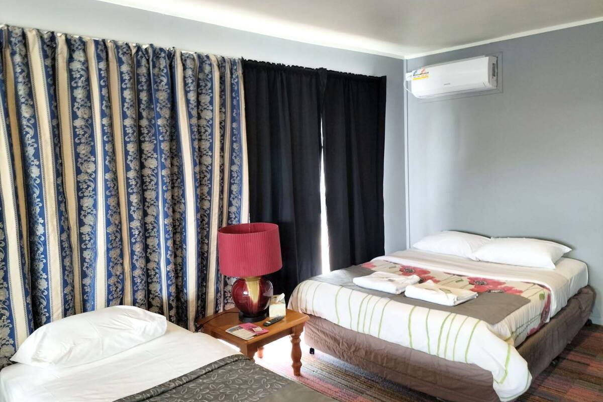 A hotel room with a bed, a bedside table with a lamp, and a window with curtains.