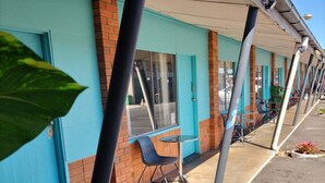 A motel with a row of rooms, each with a window and a door. There is a chair outside one of the rooms. - Maryborough Motel and Conference Center (Maryborough)