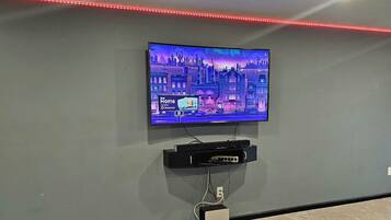 Sala de cinema com TV de tela plana na parede, projetor instalado no teto e fita de luz LED vermelha.
