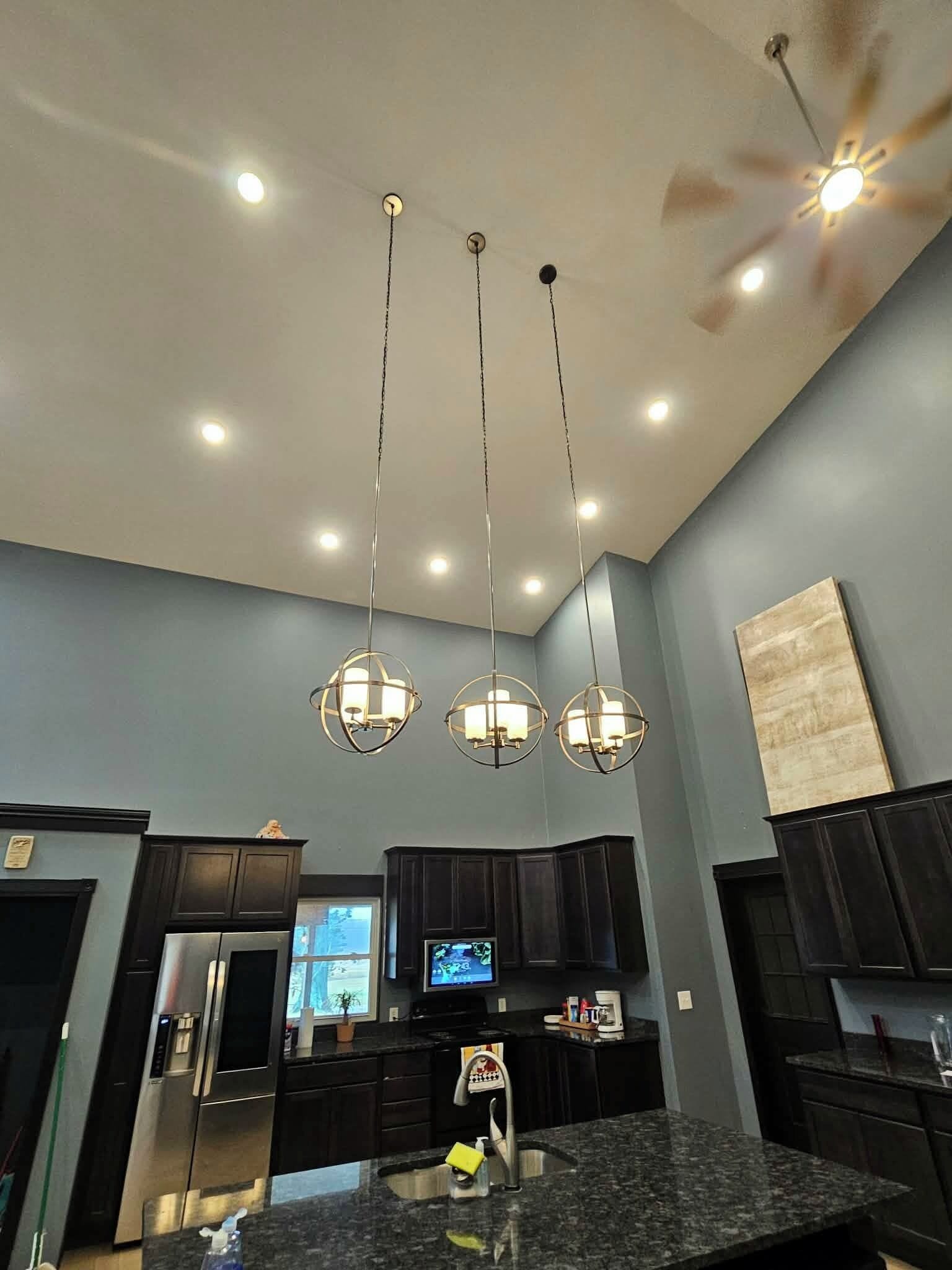 Una cucina moderna con mobili scuri, un piano di lavoro in granito, un frigorifero in acciaio inossidabile, forno integrato, una ventola a soffitto e luci a sospensione.