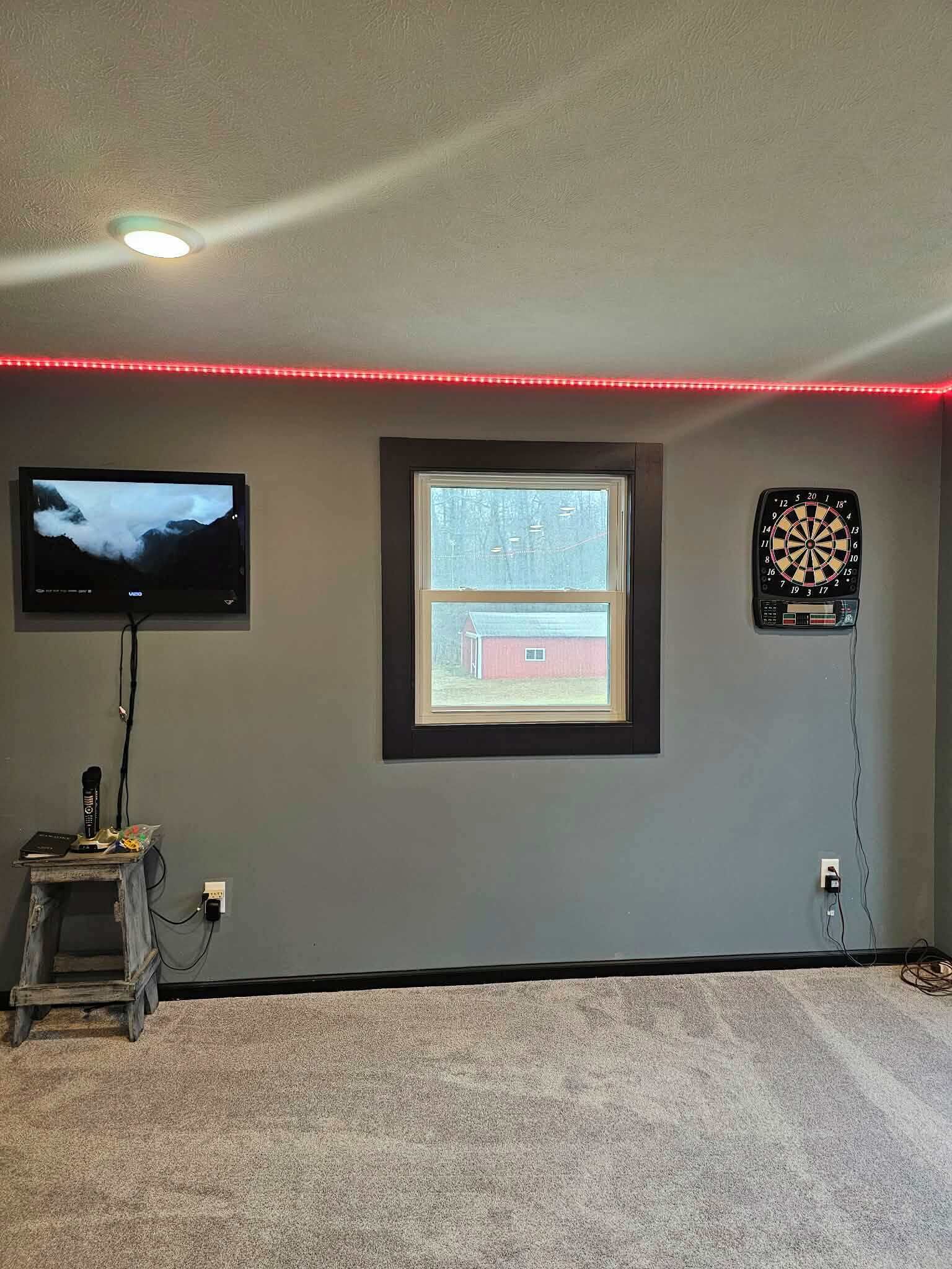 Ein Zimmer mit einem an der Wand montierten Fernseher, einem Fenster und einer Dartscheibe.