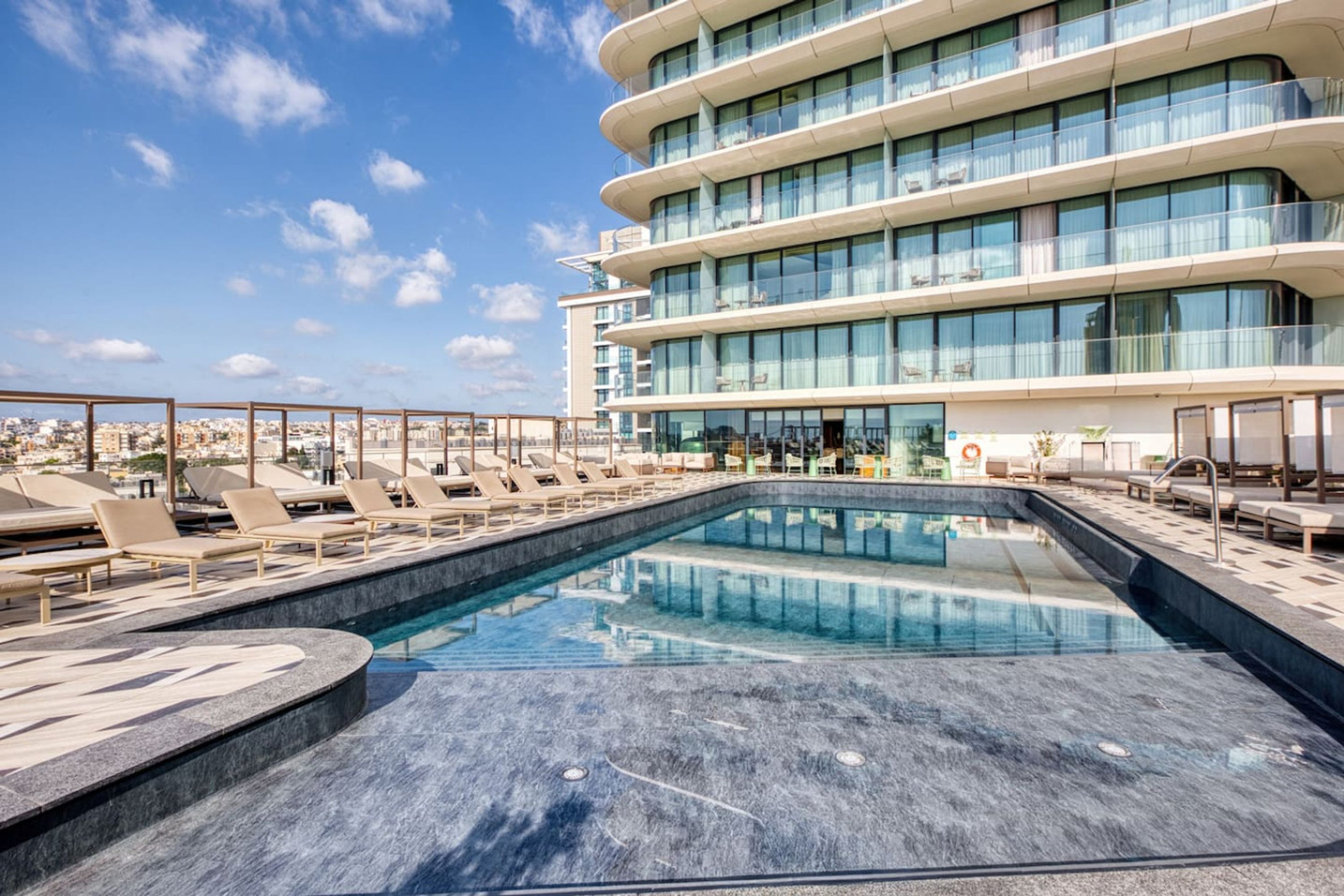 A rooftop pool area with lounge chairs and a modern building in the background.