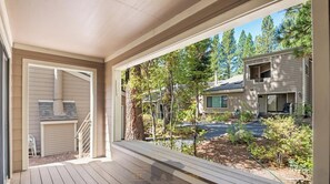 A covered porch with a view of a residential area, including a house and a driveway.
