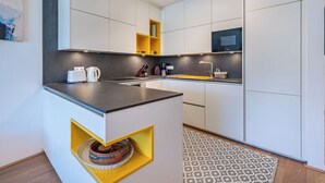 A modern kitchen with white cabinets, a black countertop, and a yellow accent shelf. - Nice apartment for 2 guests with WIFI, TV and terrace (Ossiachberg)