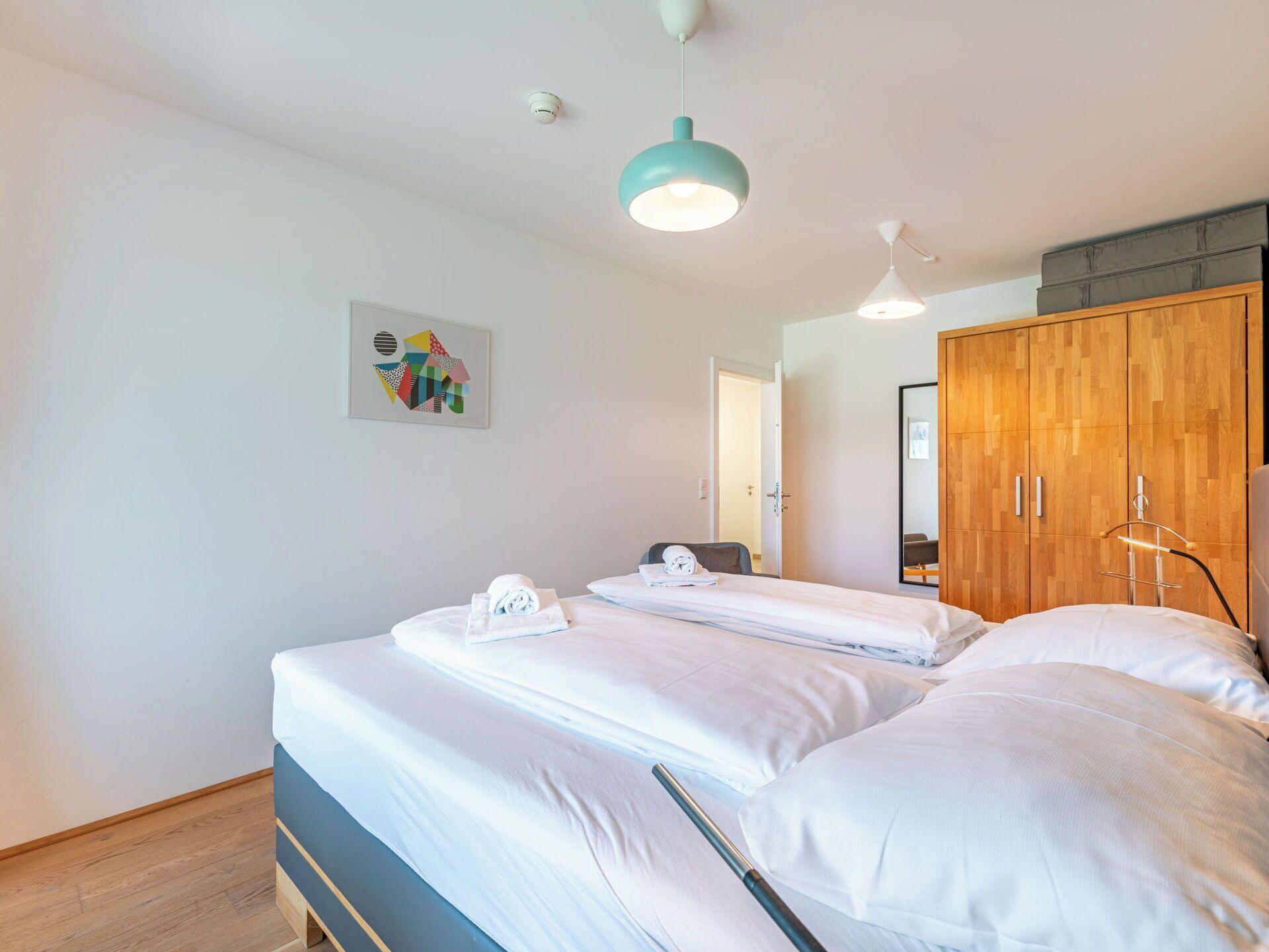 A modern hotel room with a large bed, a wooden wardrobe, and a ceiling-mounted light fixture.