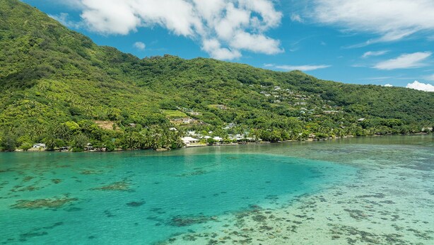 A coastal area with clear turquoise waters, a lush green hillside, and scattered buildings. - Villa Kahia by Tahiti Homes (Windward Islands)