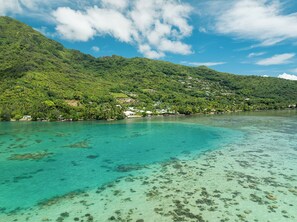 Una zona costera con aguas turquesas cristalinas, una ladera verde exuberante y edificios dispersos.