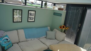 A cozy living area with a sofa, a small round table, and a sliding glass door leading to a balcony. - Atworth Haven: 4-Bed Home with Garden (Atworth)
