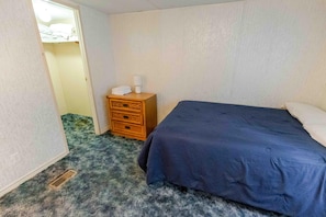 A bedroom with a single bed, a wooden nightstand with a lamp, and a door leading to another room.