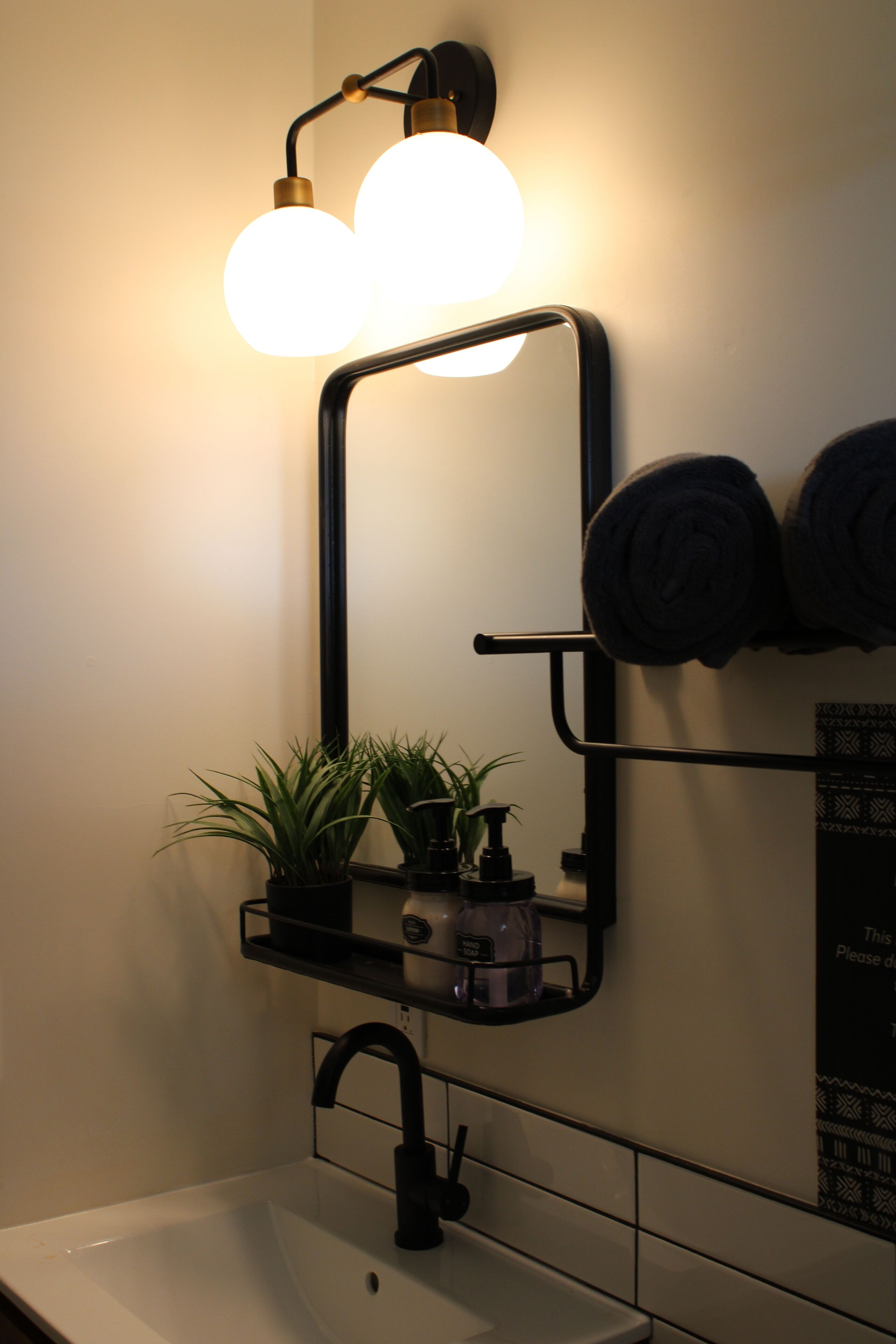A bathroom with a white sink, a black faucet, a mirror with a black frame, and a wall-mounted towel rack with rolled towels.