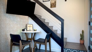 A staircase with a black handrail, a wall with framed artwork, and a small table with chairs.