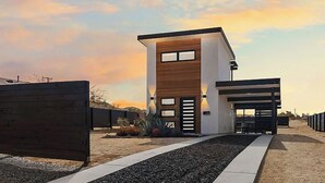 A modern two-story building with a flat roof, large windows, and a covered outdoor seating area.