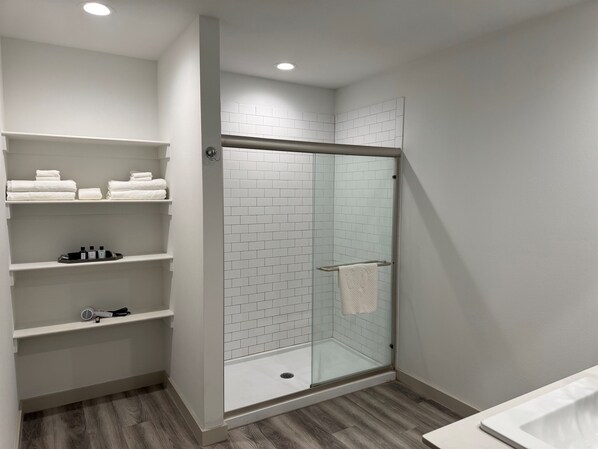 Une salle de bain moderne avec une douche à parois de verre, des murs recouverts de carreaux blancs et un plancher en bois.