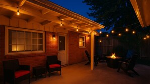 Ein Außenbereich mit einer Terrasse, Ziegelmauern, einer überdachten Sitzgelegenheit und Lichterketten.