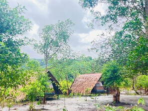A rustic outdoor setting with thatched-roof huts surrounded by dense greenery.